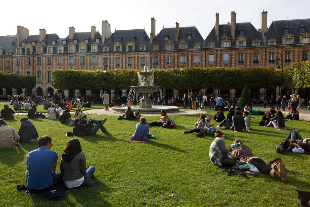 Visitors of the square relaxing on the grass near a fountain in the Marais district